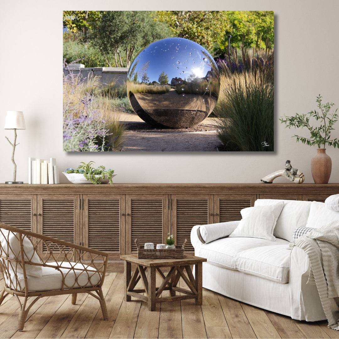 Casual farmhouse style decor with off white couch and wooden cabinet. Above the cabinet is a large wall art decor of the hall gazing ball in California.