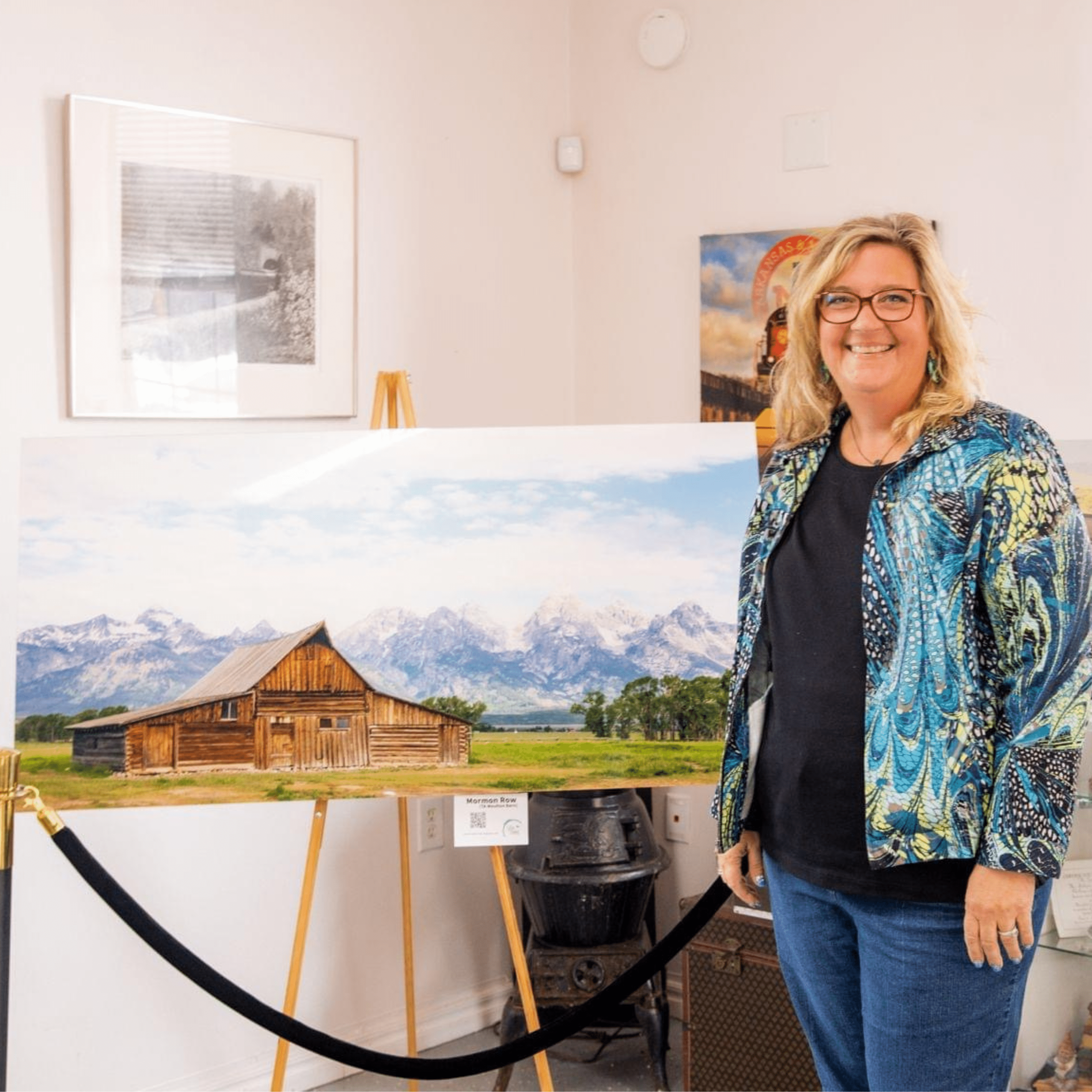 Artist Lisa Blount standing beside a large TA Moulton Barn fine art print displayed on an easel during an exhibition.