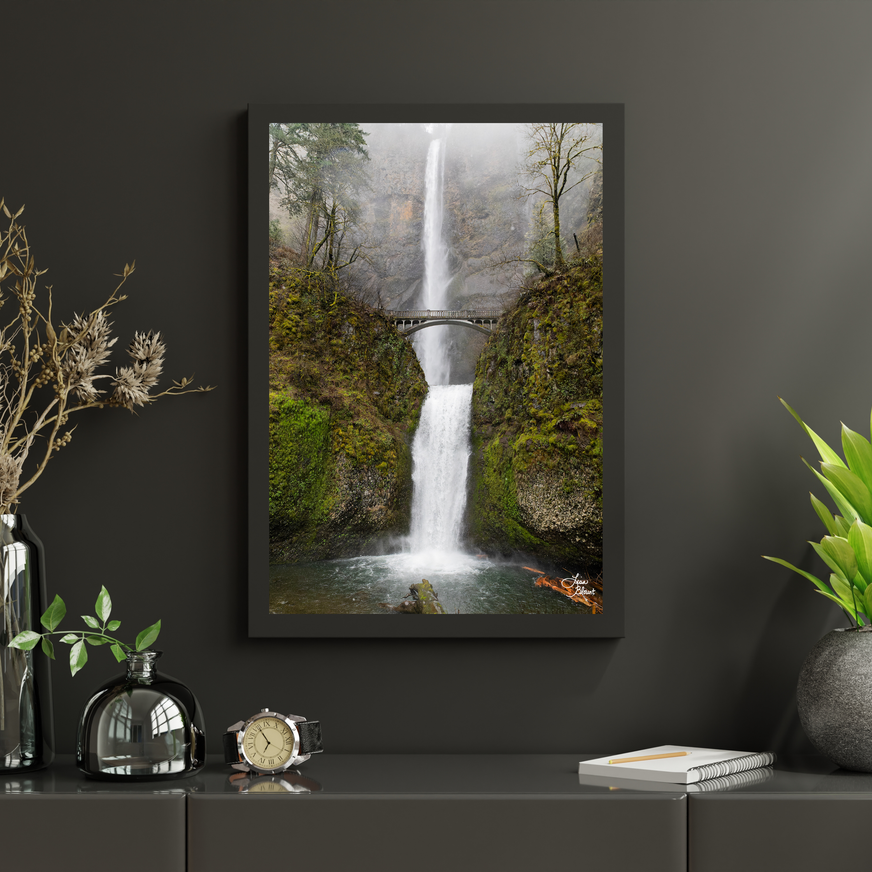 Framed Multnomah Falls wall art styled on a dark charcoal wall above a decorative console, surrounded by greenery and glass accessories.