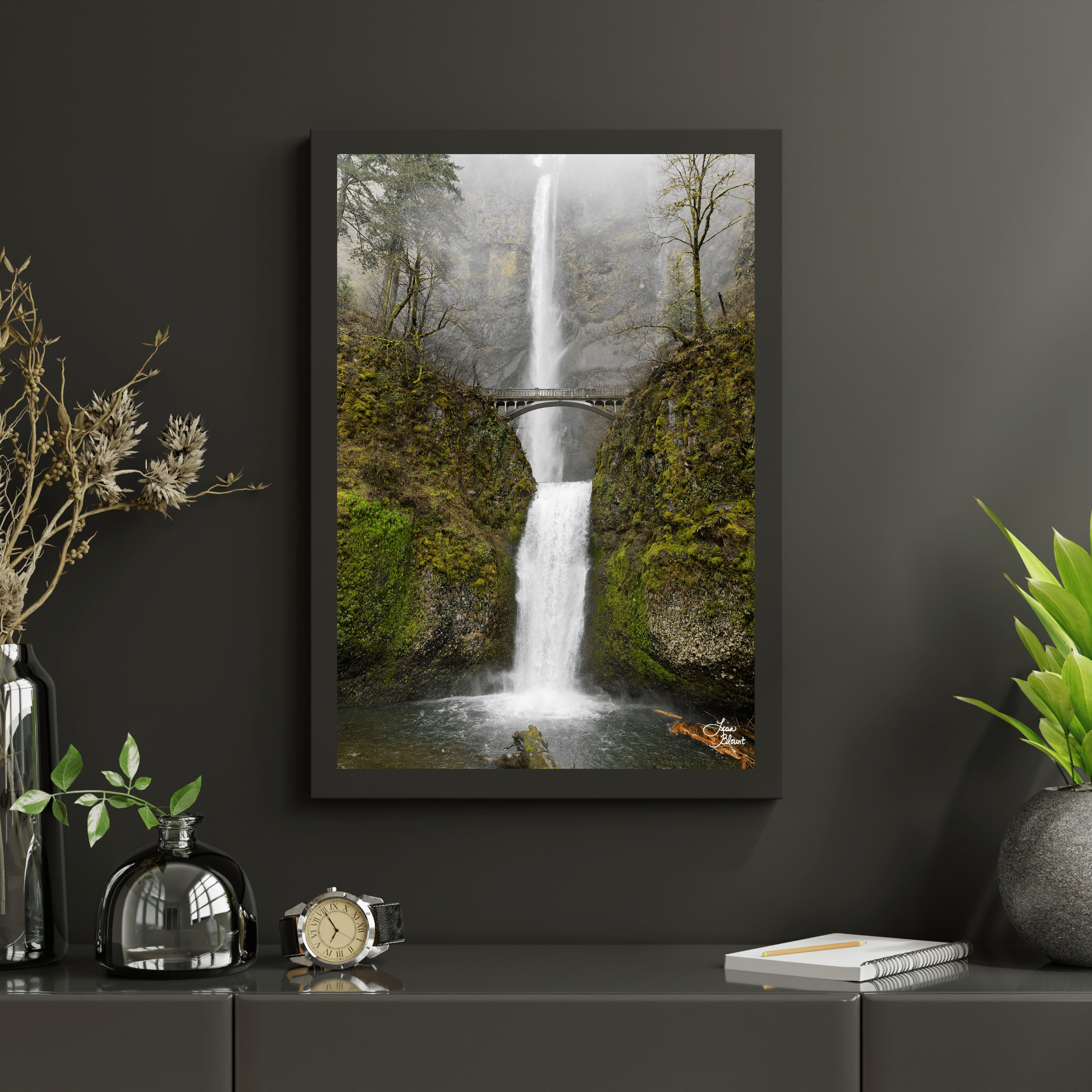 Framed Multnomah Falls wall art styled on a dark charcoal wall above a decorative console, surrounded by greenery and glass accessories.
