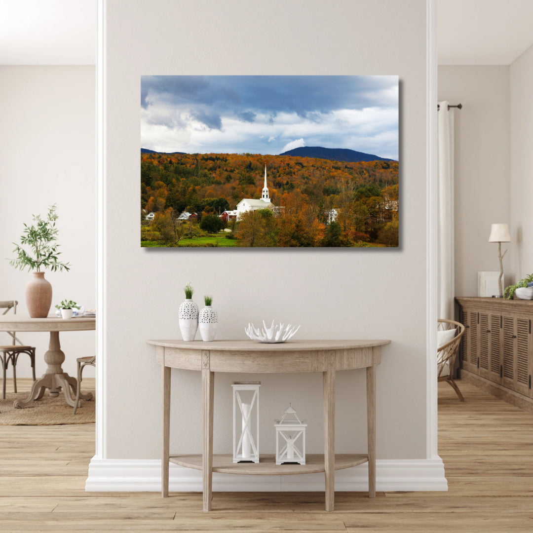 Stowe Vermont’s white church in the fall with orange leaves. Large 30x20 canvas print featured in a a hallway of what could be neutral or farmhouse colors.