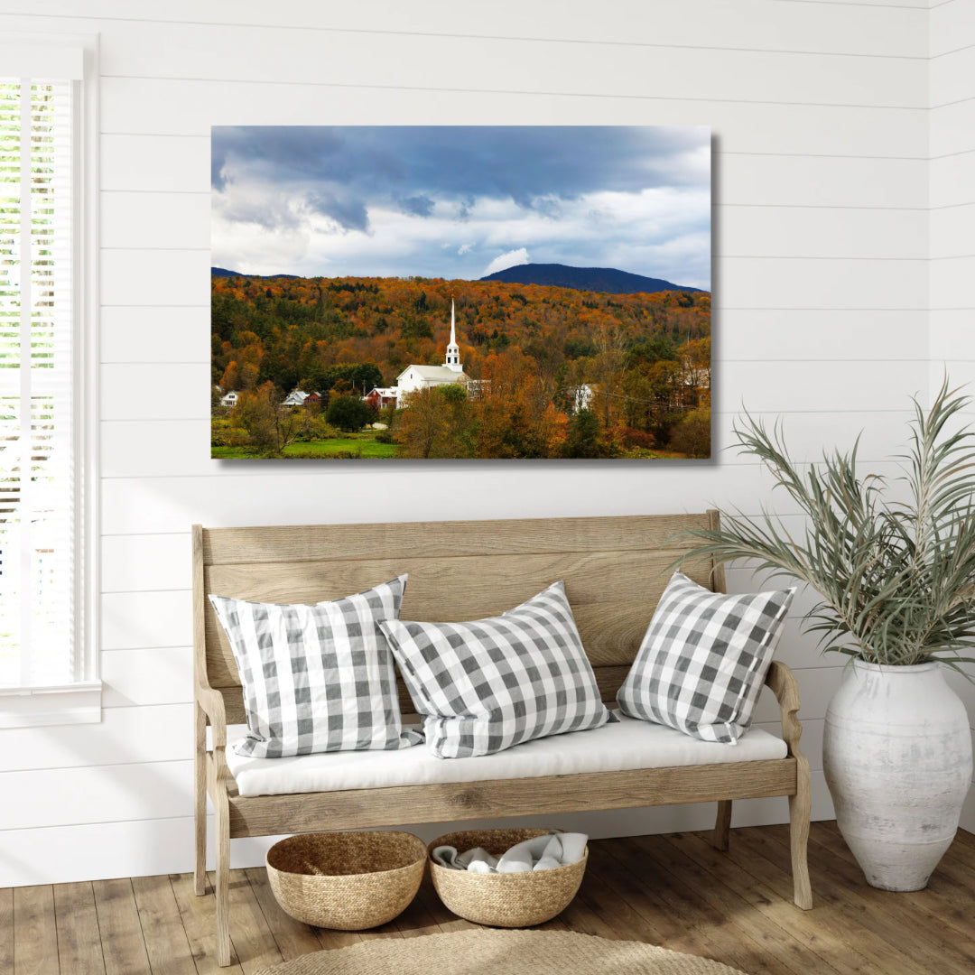 Stowe Vermont’s white church in the fall with orange leaves. Art is hanging above a farmhouse style bench in a hallway or entryway with checkerboard pillows on the bench.