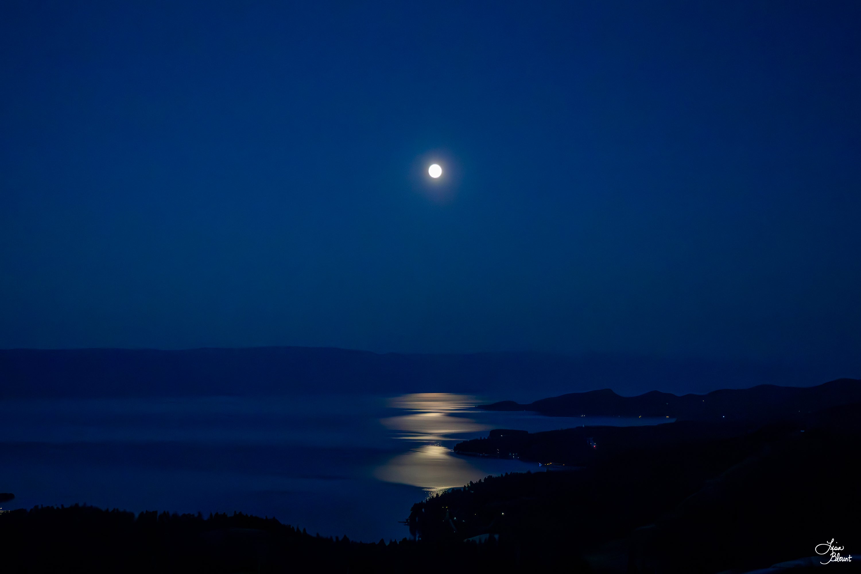 Moonlight over Flathead Lake in Somers, Montana with a silver reflection across deep blue water – fine art photography wall art.