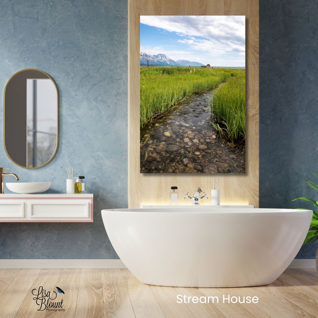 Grand Teton wall art featuring a stream, rustic barn, and mountain landscape at Mormon Row styled above a freestanding tub in a calming bathroom