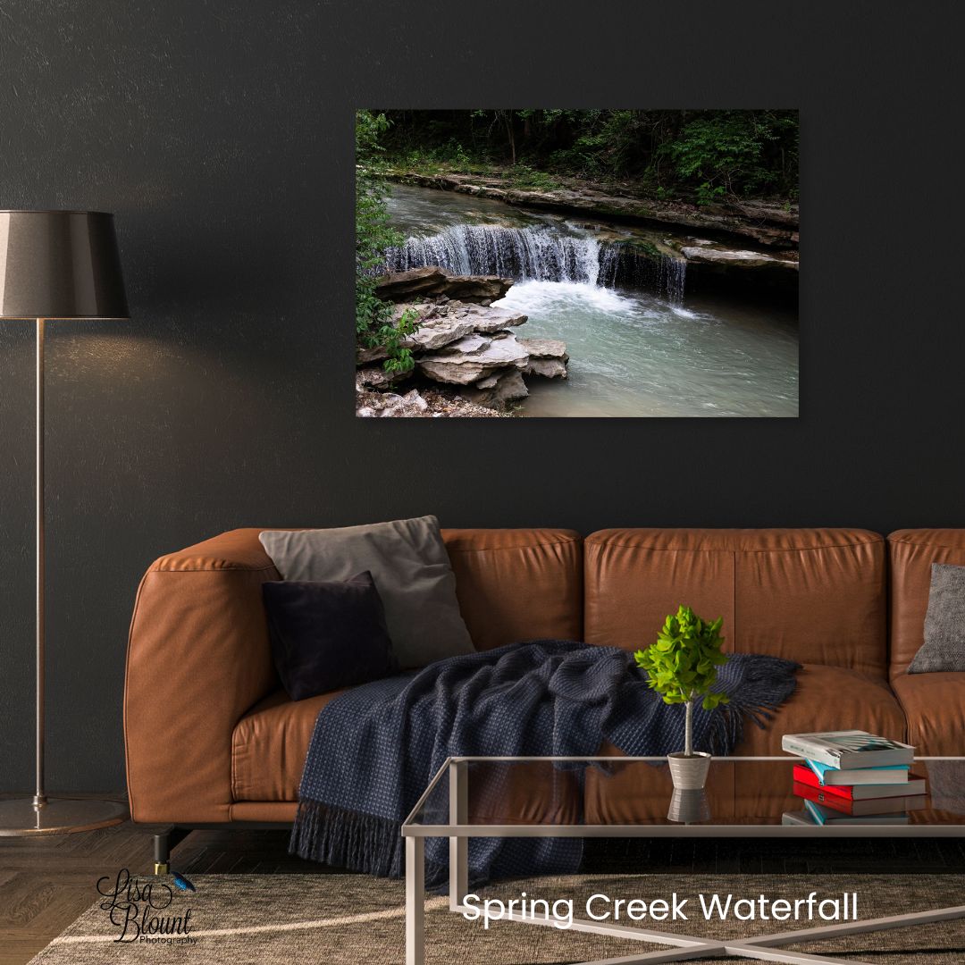 Arkansas waterfall wall art displayed above a leather couch featuring Spring Creek Waterfall with layered rock, moving water, and peaceful woodland greens.