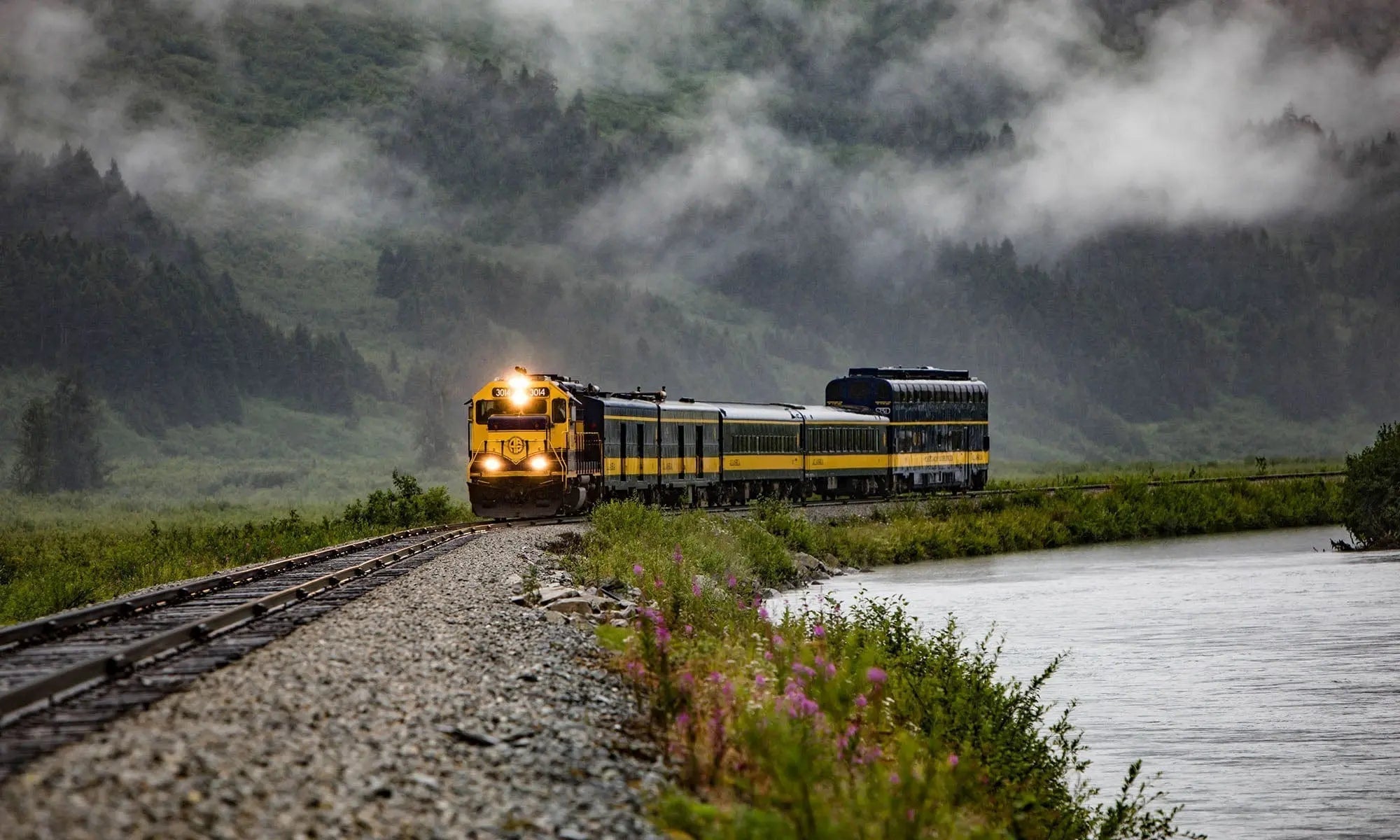 Limited edition fine art photograph of the Glacier Discovery Train winding through Alaska’s misty mountain valley—golden locomotive, river, and forest scenery.