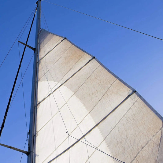 View of someone relaxing on a sailboat looking up the sail towards the blue sky