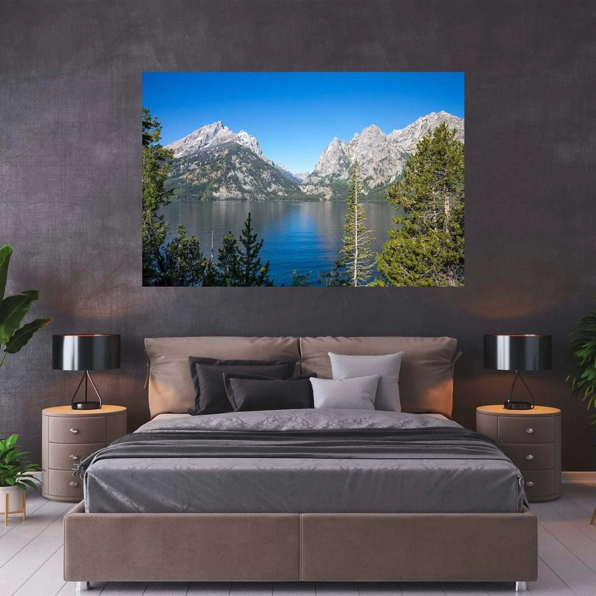 Large Jenny Lake wall art of the Teton Mountains and lake shoreline hanging above a modern gray bedroom bed with plants and warm lighting.