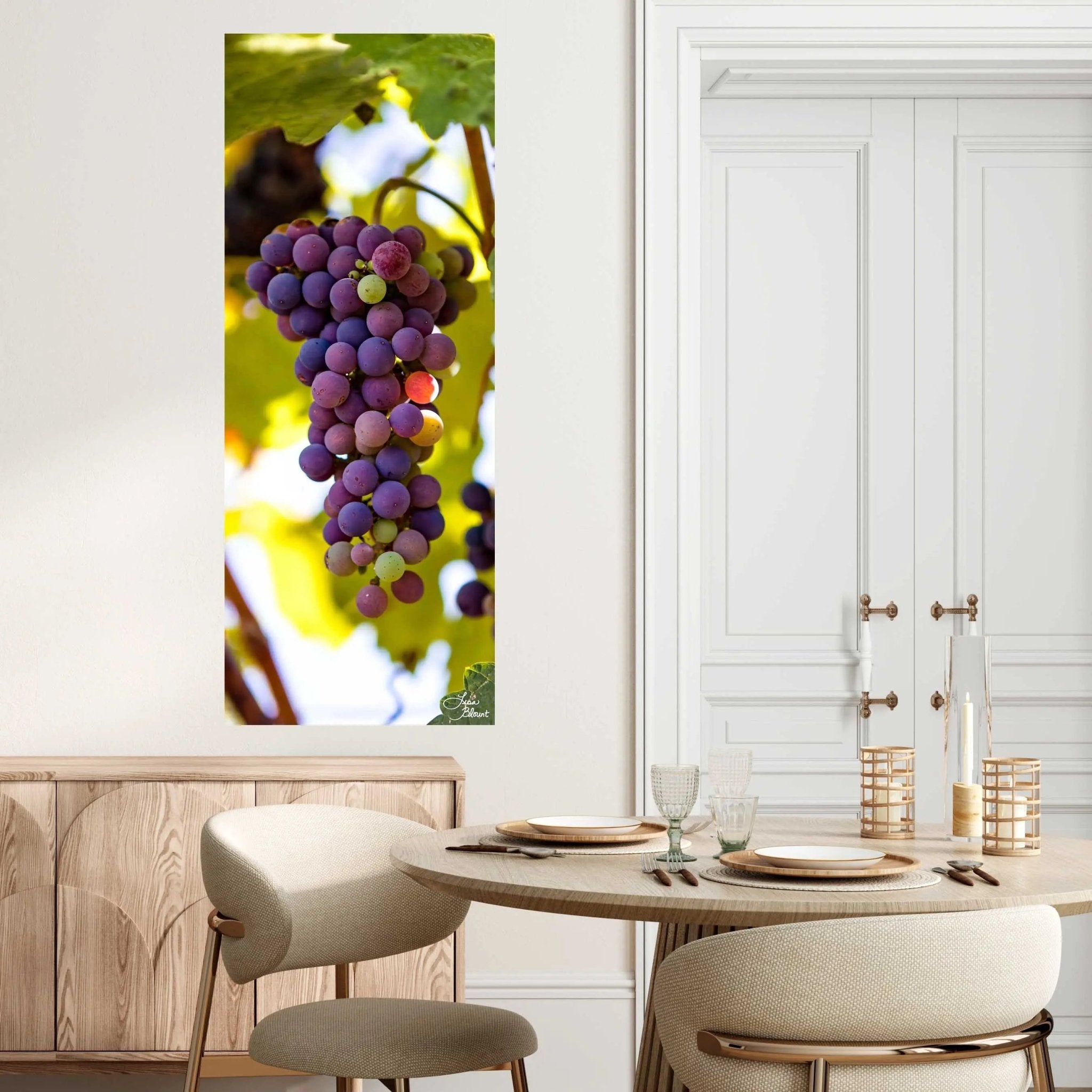 Large vertical wall art of Napa Valley grapes displayed in a modern dining room with cream chairs and gold-accented table decor.