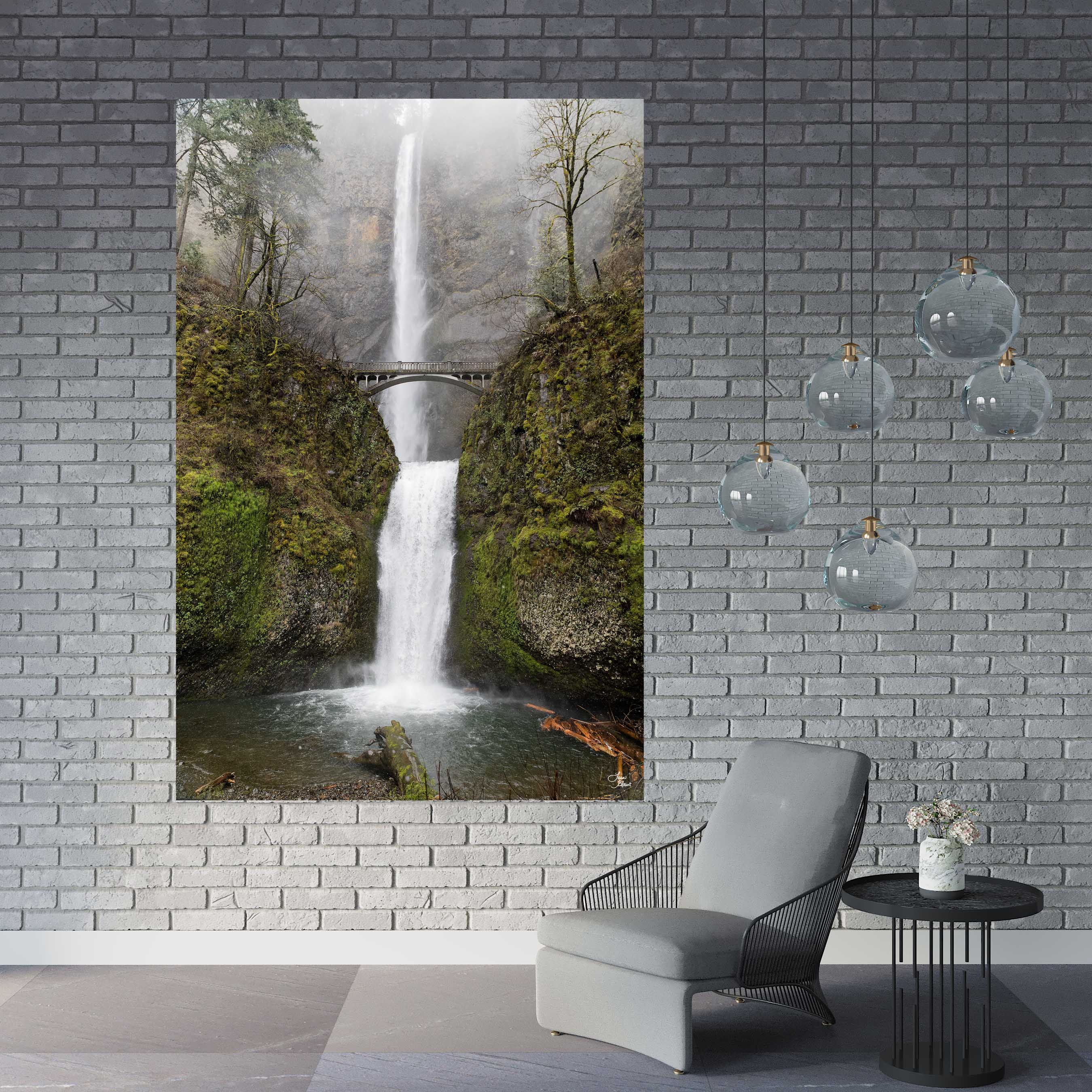 Large Multnomah Falls wall art on a gray brick accent wall with glass pendant lights and a soft lounge chair, styled in a modern interior.