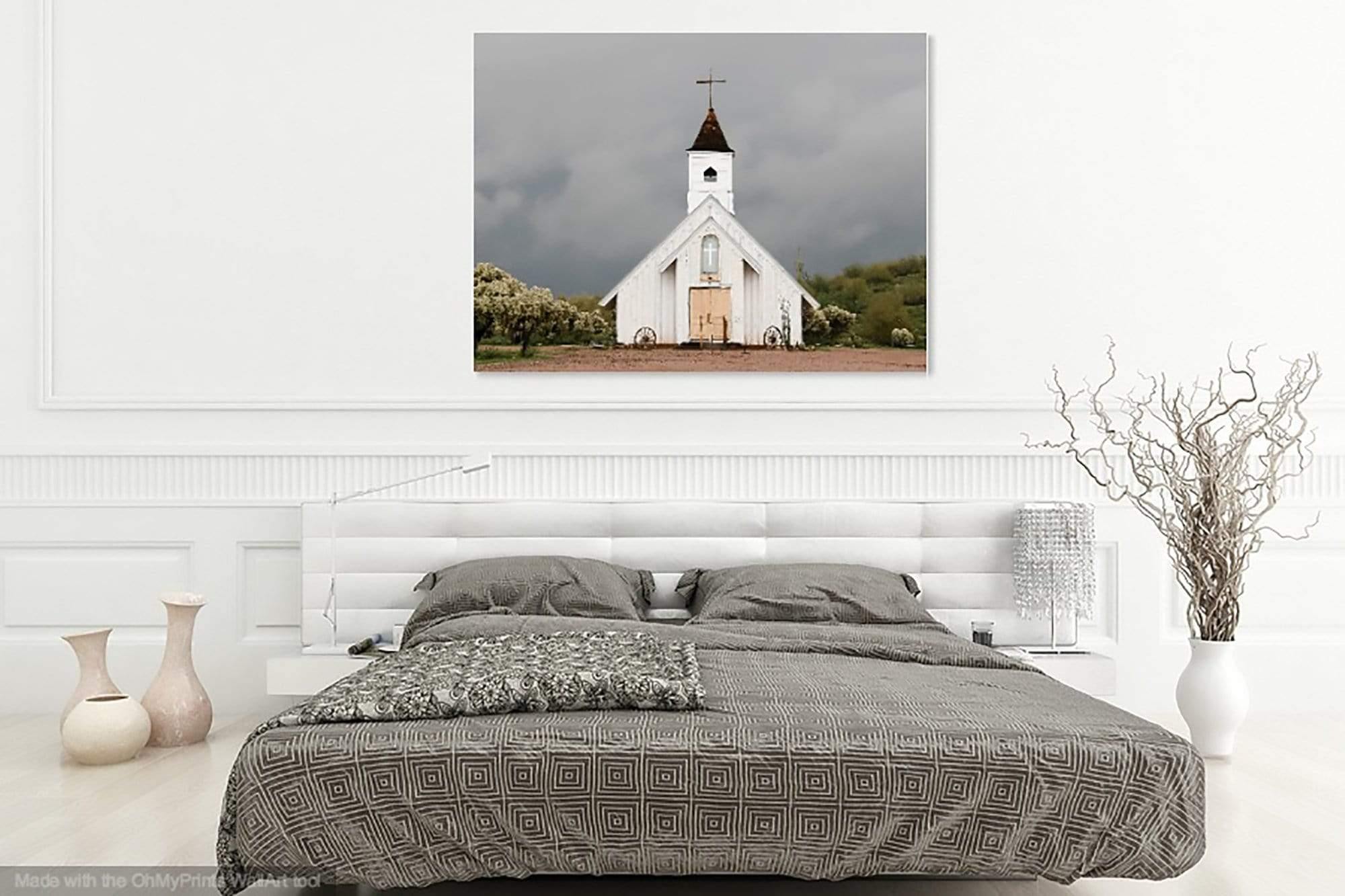 White rustic church photograph “Spiritual Warfare” hanging above a clean, minimalist bedroom with neutral bedding.