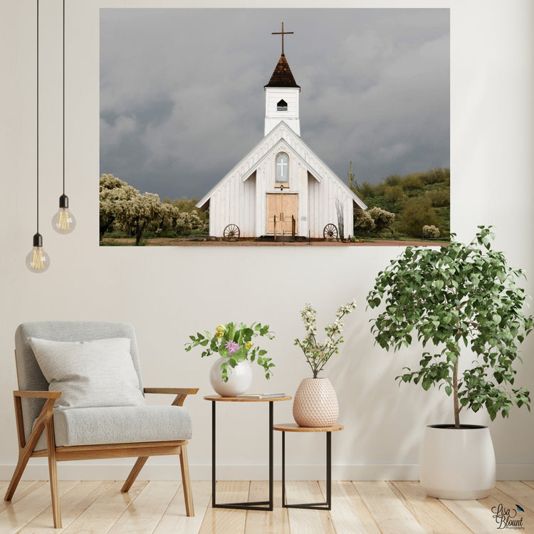 Rustic country church home decor focused on comparing light and dark with white church and dark clouds. Titled Spiritual Warfare this fine art hangs in a sitting area on a white wall.