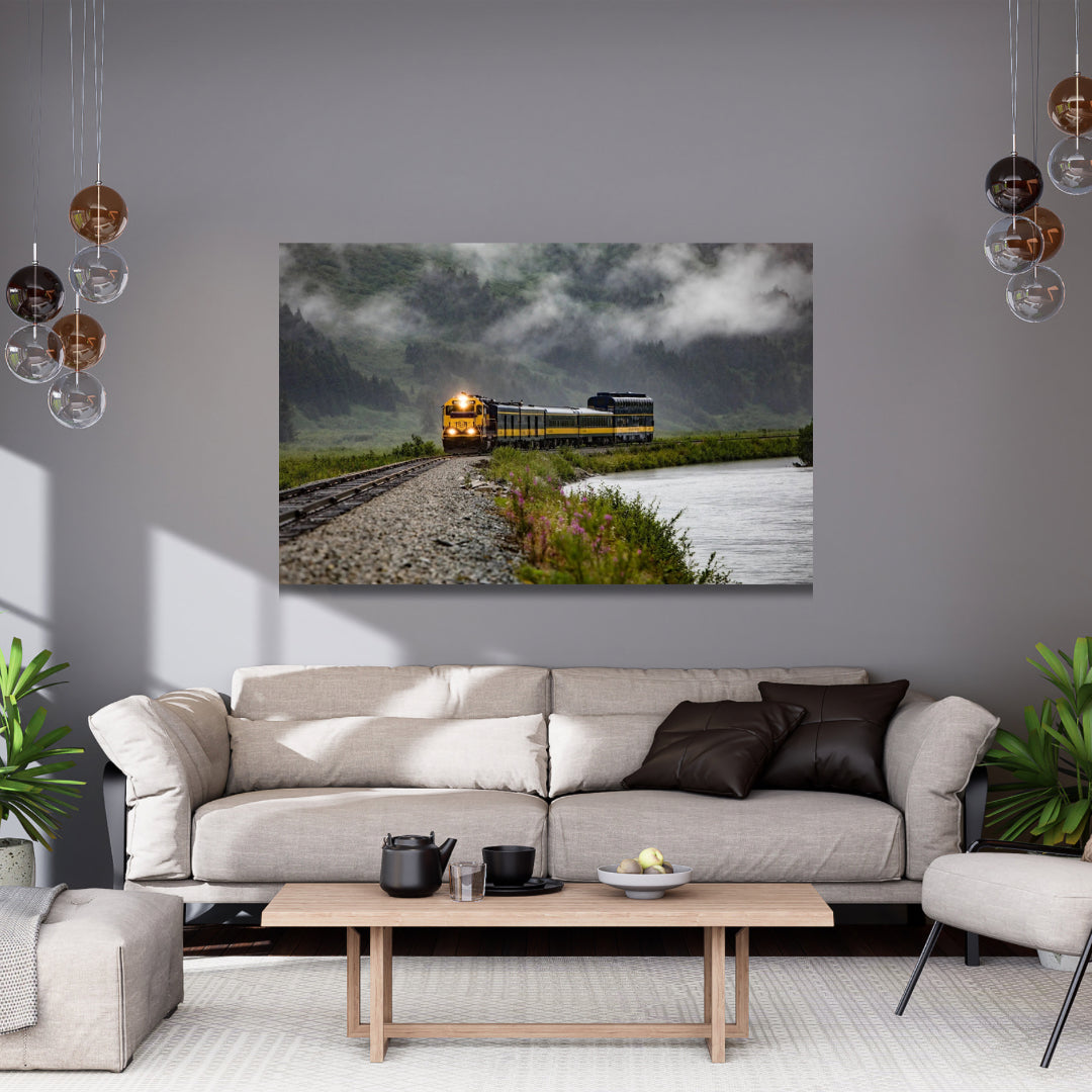 Large landscape photo of a blue yellow train coming towards you set in cloud covered mountains hanging in a gray living room
