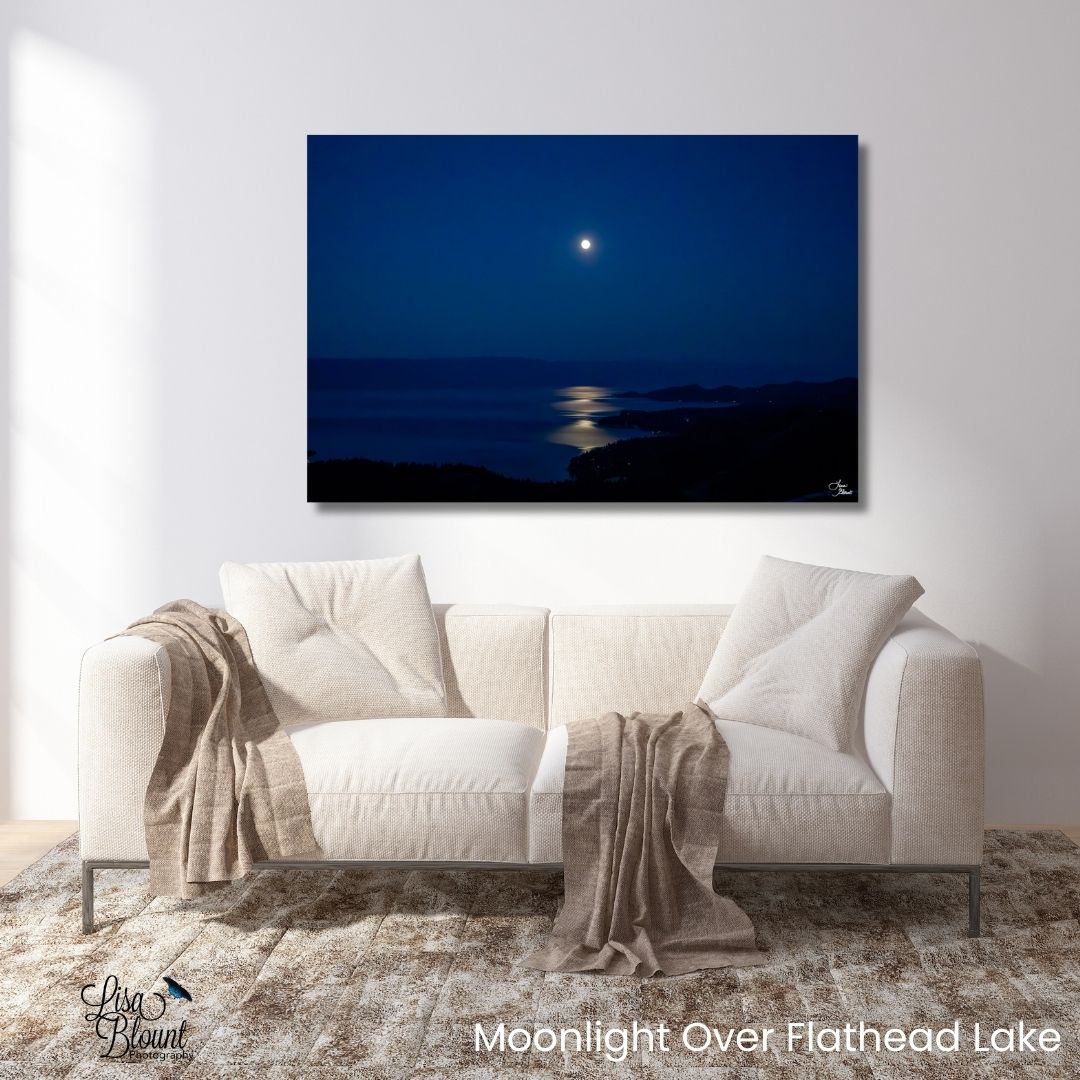 White sofa with beige throw blankets in a room with a large wall-mounted painting of a Moonlight over Flathead Lake in Somers, Montana with a silver reflection across deep blue water – fine art photography wall art.