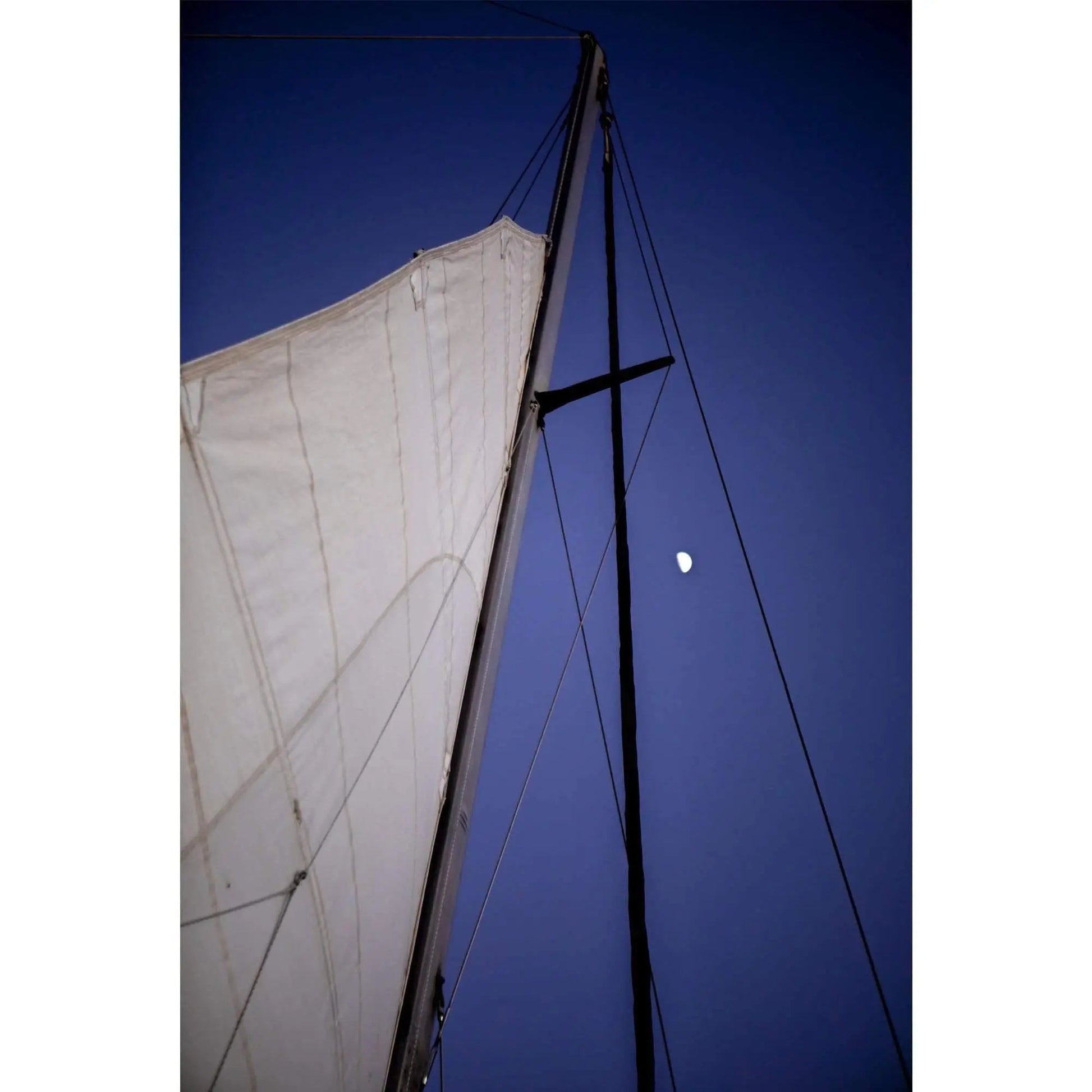 Night time sail mast surrounds moon light in dark blue