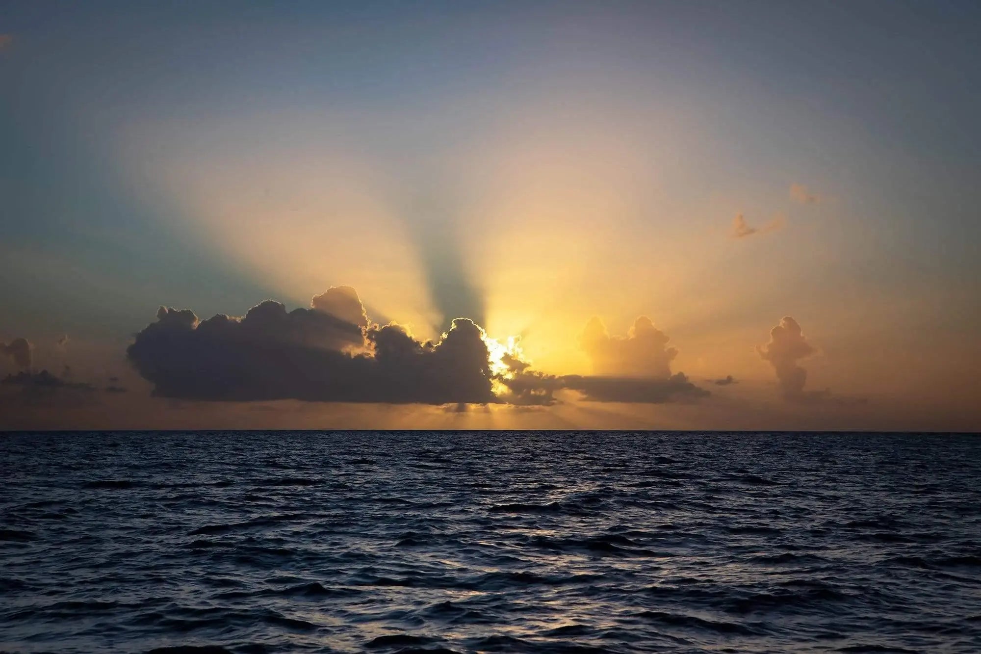 Escape to paradise sunburst of sunset over ocean half hidden behind a cloud