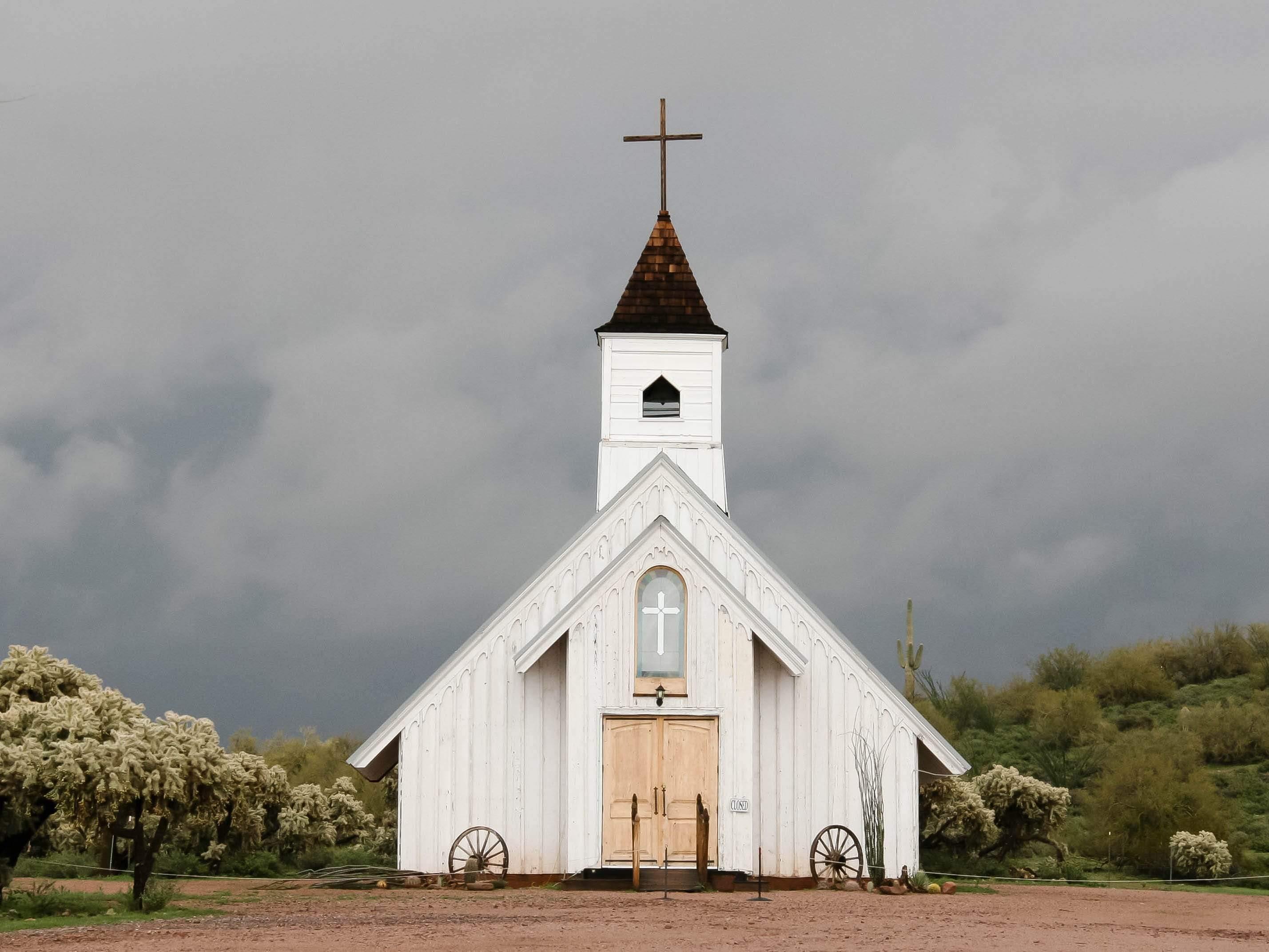 White church glowing against a desert storm near Superstition Mountain – fine art photograph capturing light breaking through darkness.